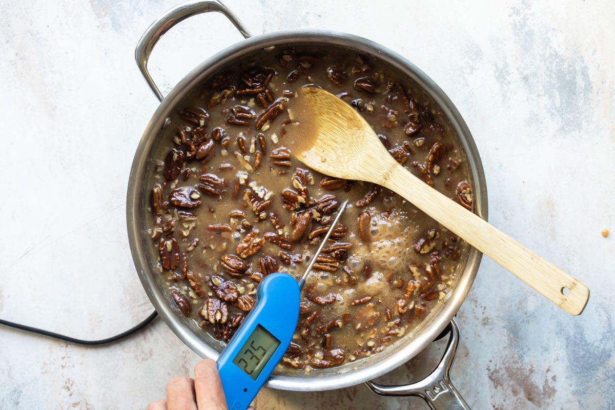 Pecan praline mixture being temped in a silver pan with a wooden spoon resting in it.