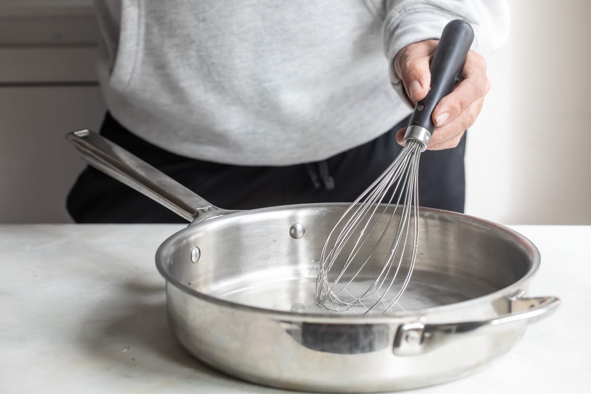 A clear liquid being whisked in a silver pan.