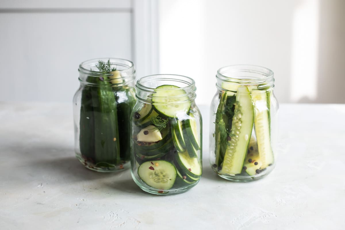 Three mason jars with ingredients for pickles in them.