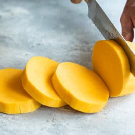 Peeled butternut squash being sliced into rounds.