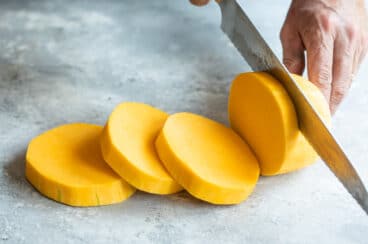 Peeled butternut squash being sliced into rounds.