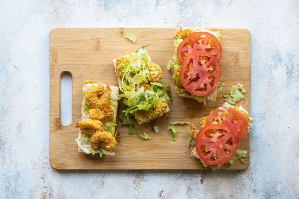 Shrimp po' boy sandwiches being assembled on a wooden cutting board.