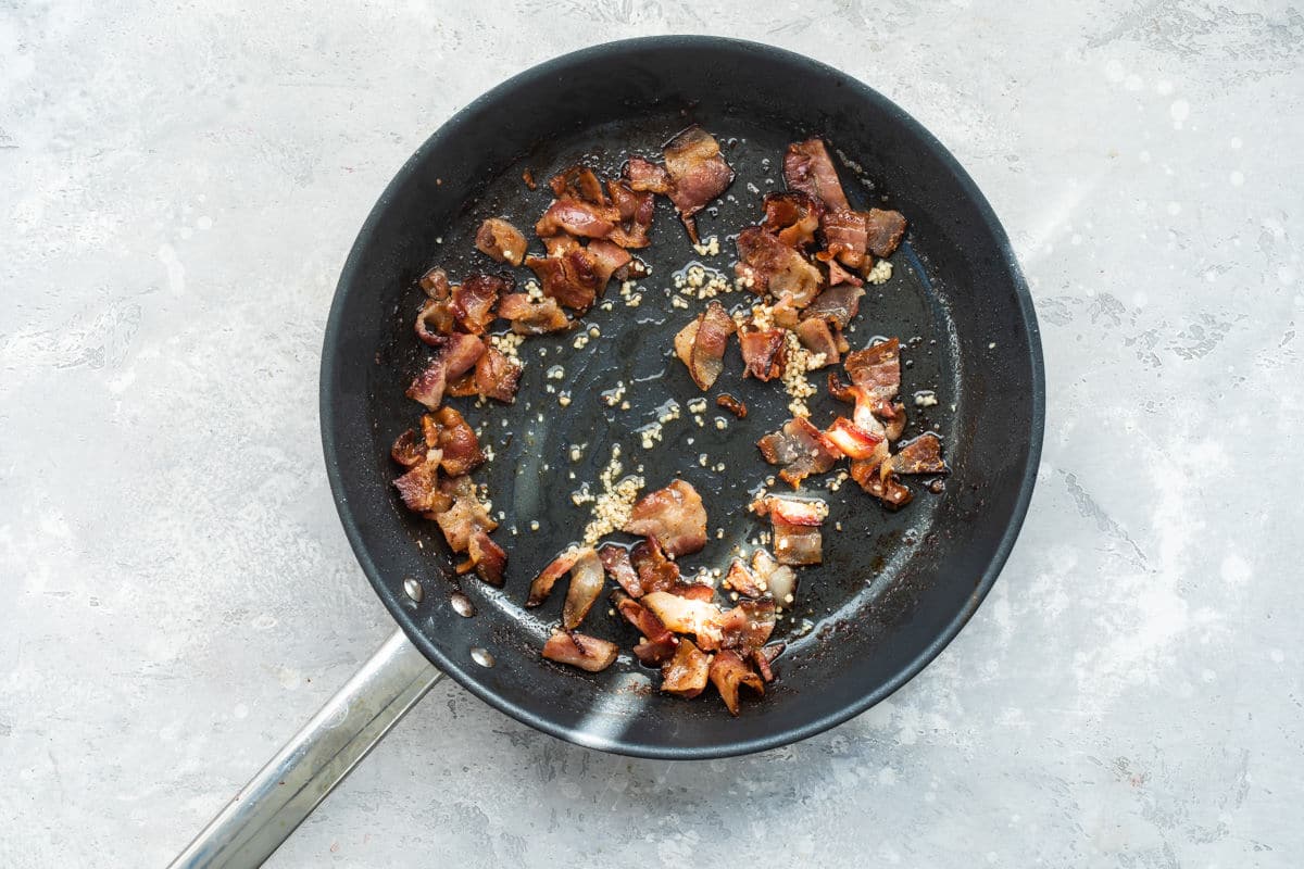 Bacon and garlic cooking in a black skillet.