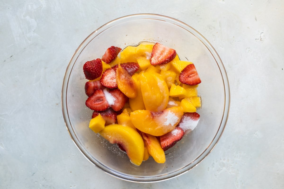 Fruit for white sangria in a clear bowl with sugar on top.