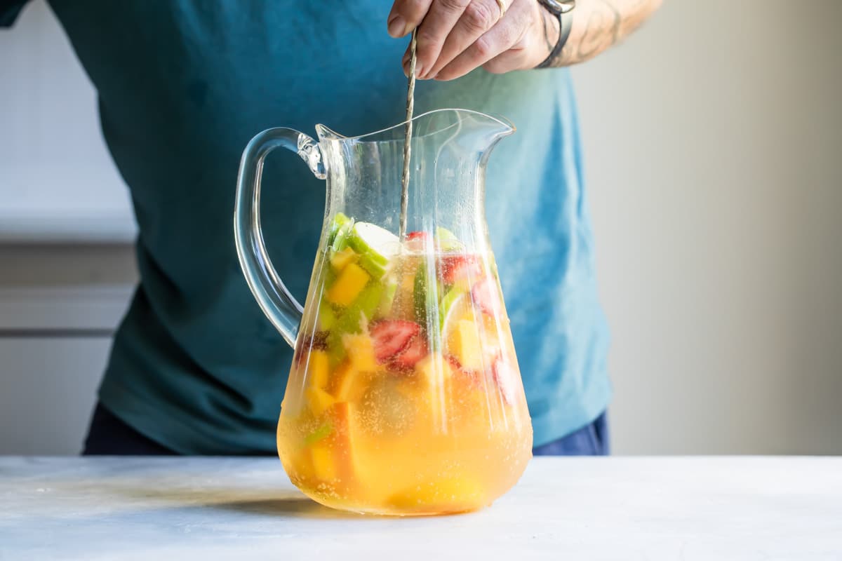 Someone stirring a pitcher of white sangria.