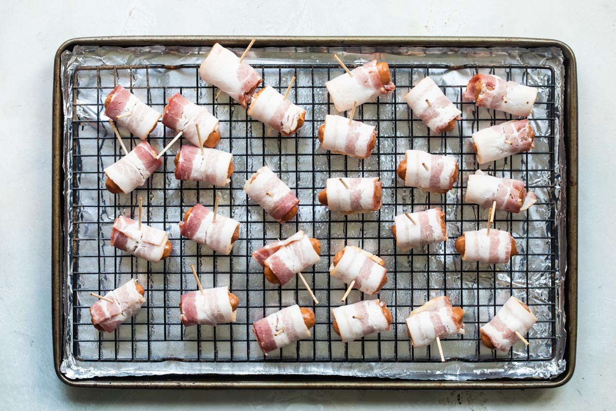 Bacon wrapped smokies on a cooling rack over a foil covered baking sheet before being cooked.
