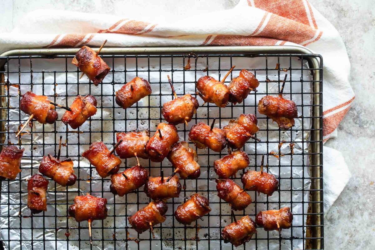 Bacon wrapped smokies on a cooling rack over a foil covered baking sheet.