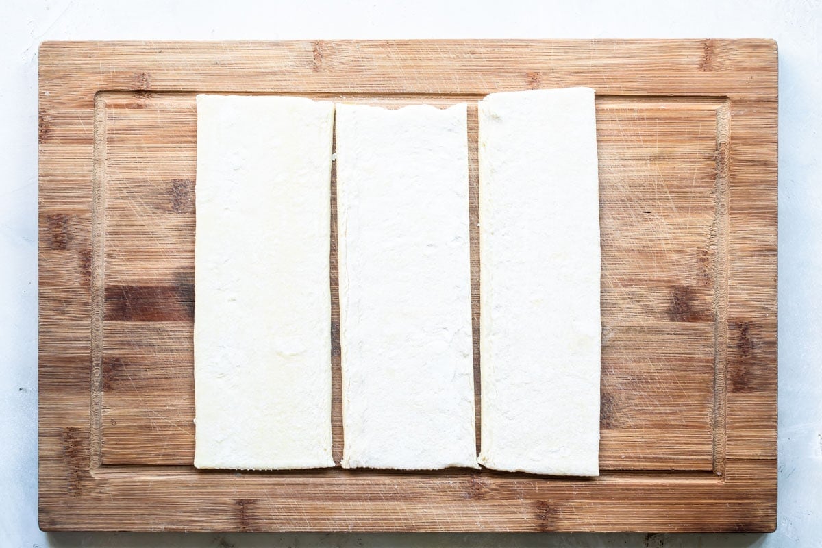 Three sheets of croissant dough spread out on a wooden cutting board.