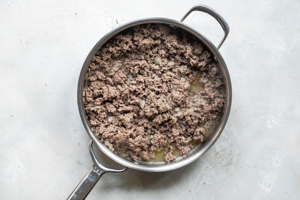 Ground beef and onions in a silver skillet.