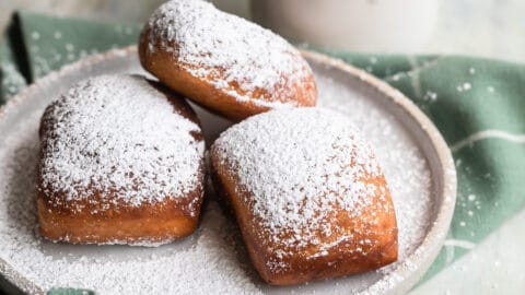 Beignets on a plate next to a coffee mug with liquid in it.
