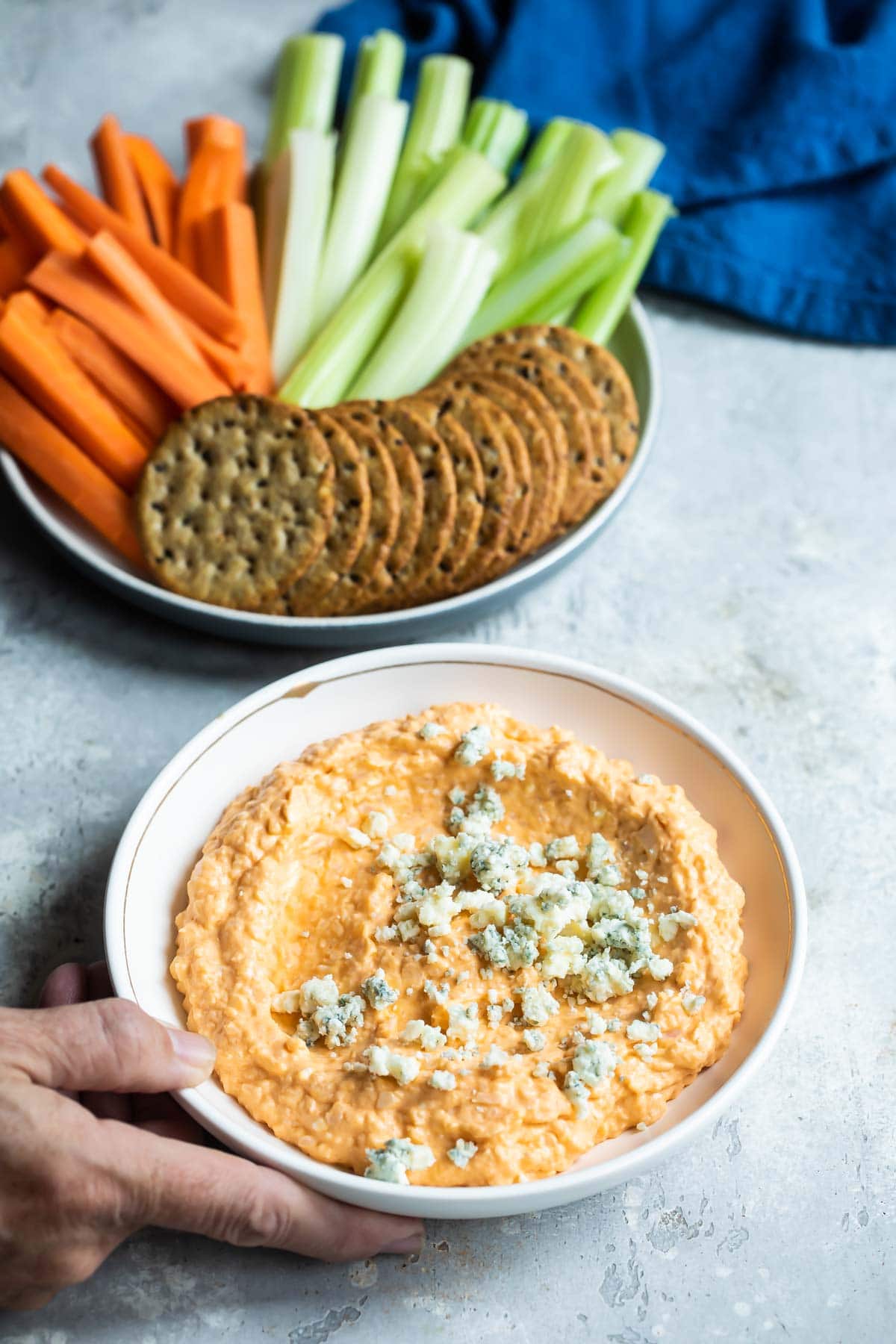 Cauliflower buffalo dip in a bowl next to a bowl of carrots, celery and crackers.