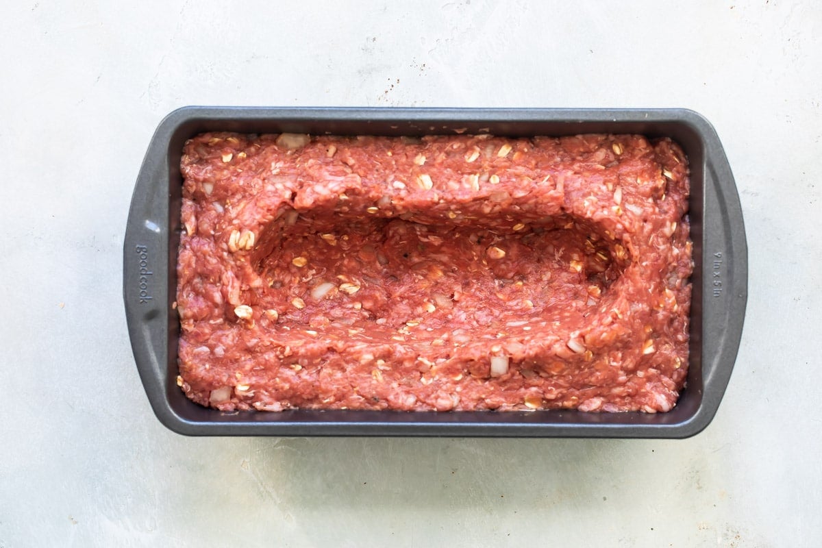 Meatloaf mixture in baking pan with a well for cheese dug out.