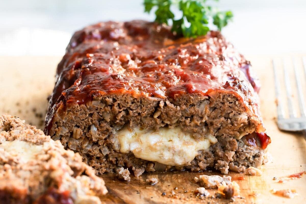 Cheesy meatloaf on a wooden cutting board.