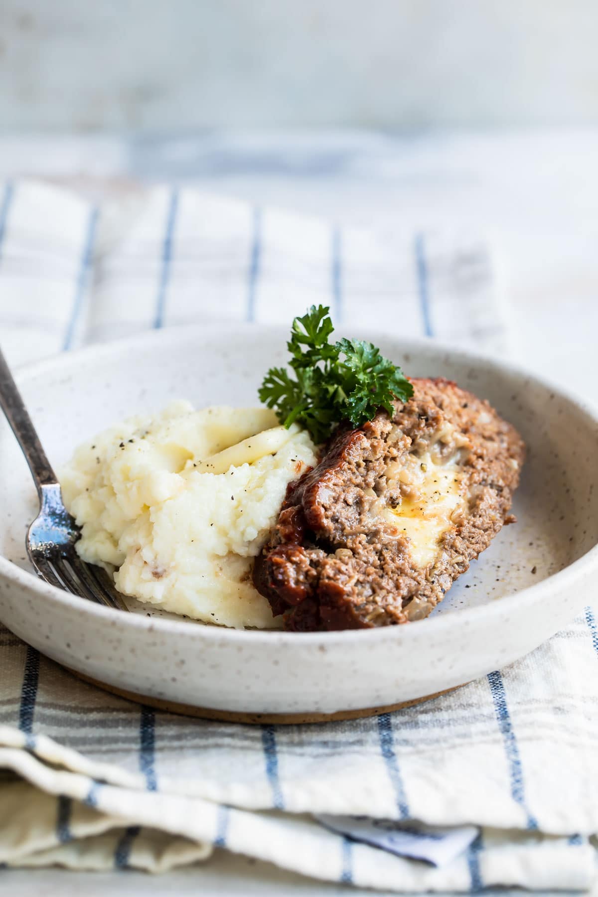 A slice of cheesy meatloaf with mashed potatoes in a low gray bowl.