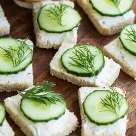 Cucumber sandwiches on a round wooden platter.