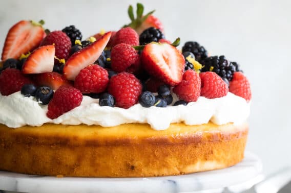 Lemon cake with limoncello cream and berries on top on a marble cake stand.
