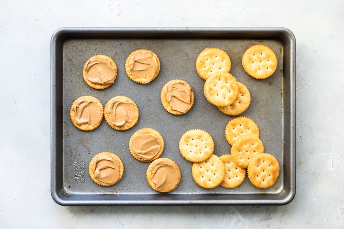 Ritz crackers on a baking sheet, half topped with peanut butter.