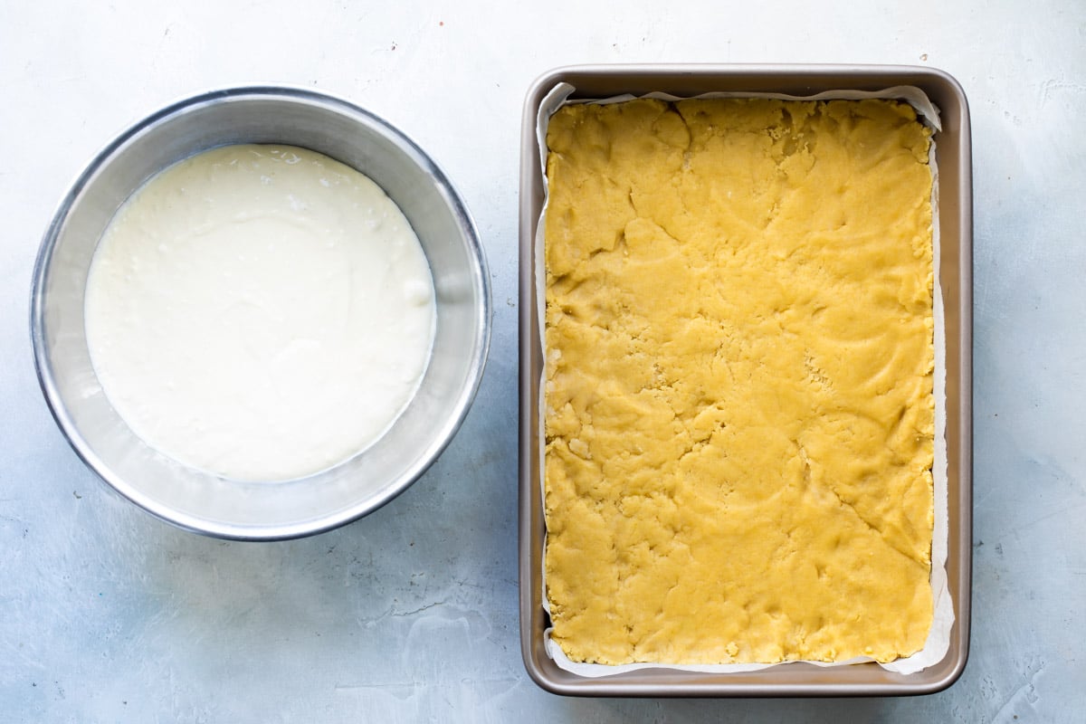 Cheesecake filling next to a pan of pressed cookie dough.