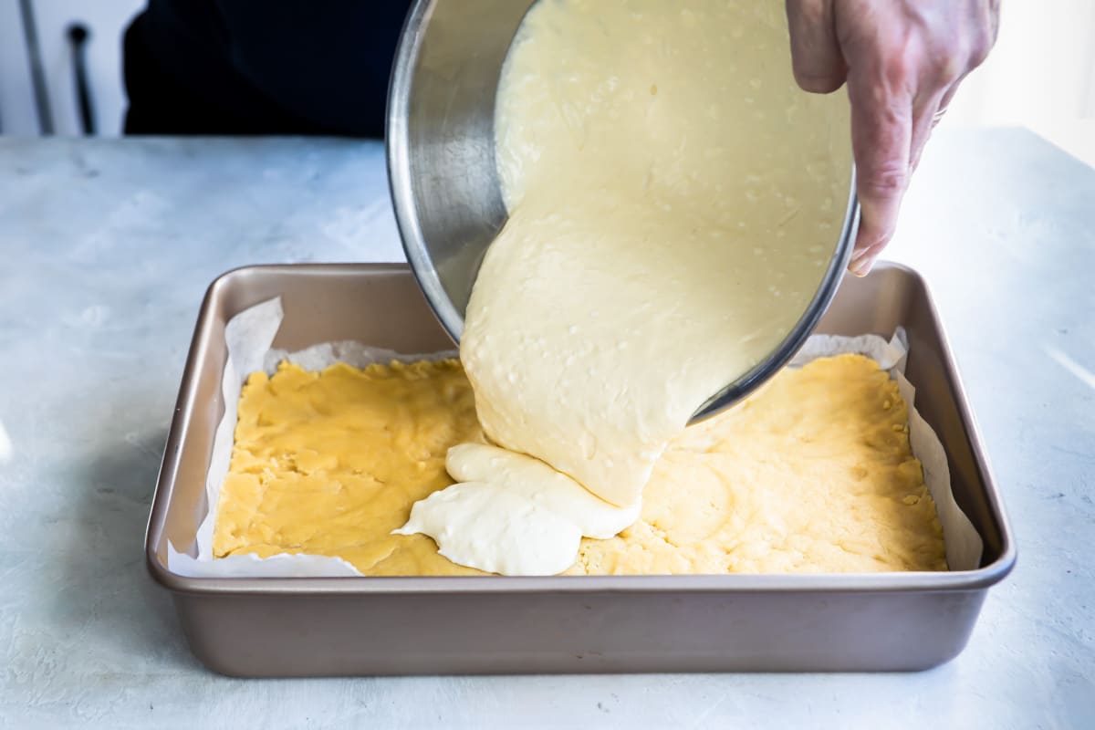 Cheesecake mixture being poured on top of sugar cookie dough.