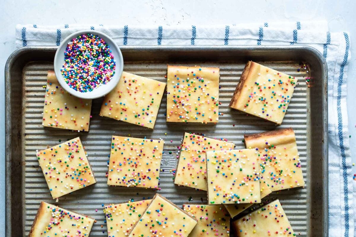 Sugar cookie cheesecake squares on a baking sheet.