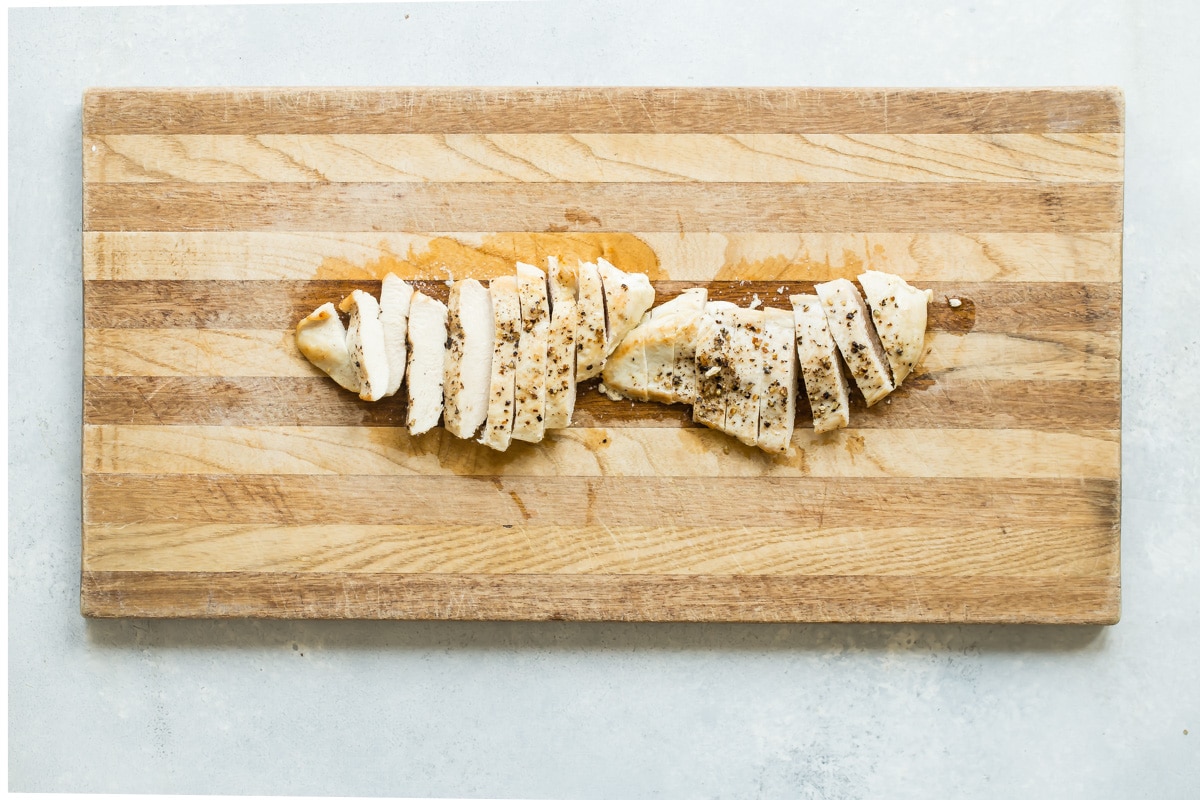 Cooked chicken breast sliced on a wooden cutting board.