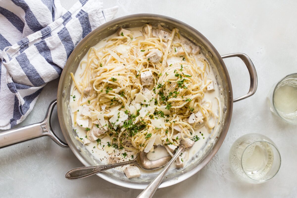Chicken alfredo in a silver skillet with a spoon and fork.