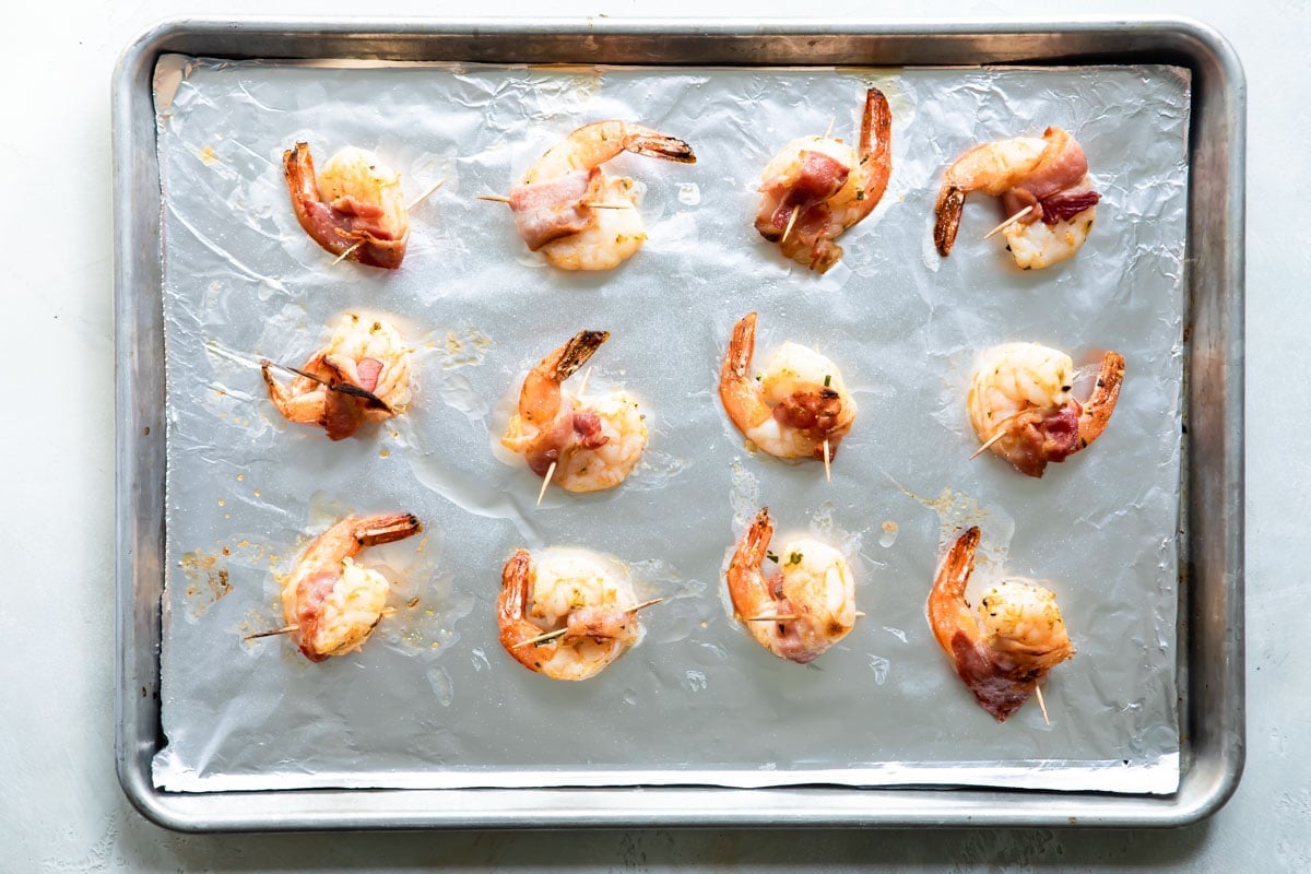 Bacon wrapped shrimp on a baking sheet before being cooked.