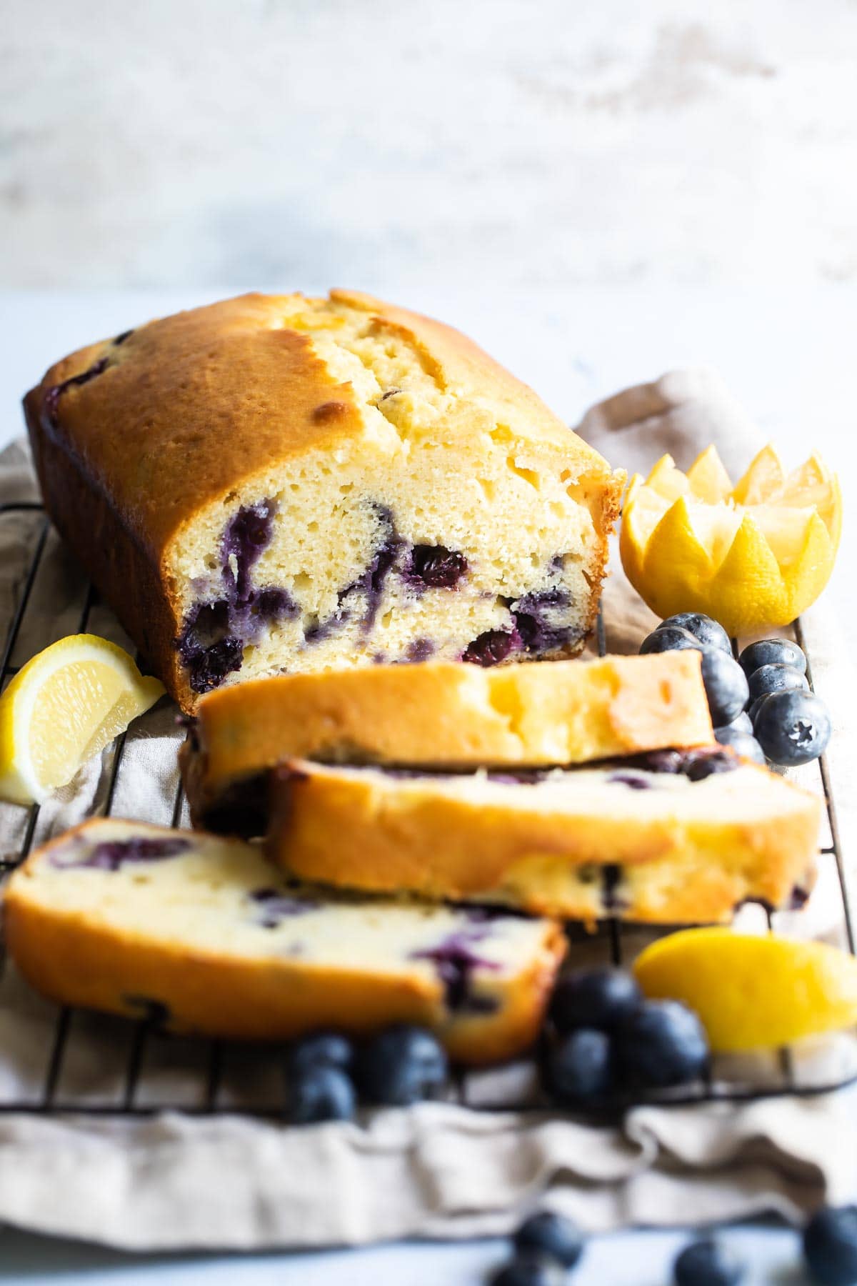 A loaf of blueberry lemon yogurt cake with three slices cut on a cooling rack.