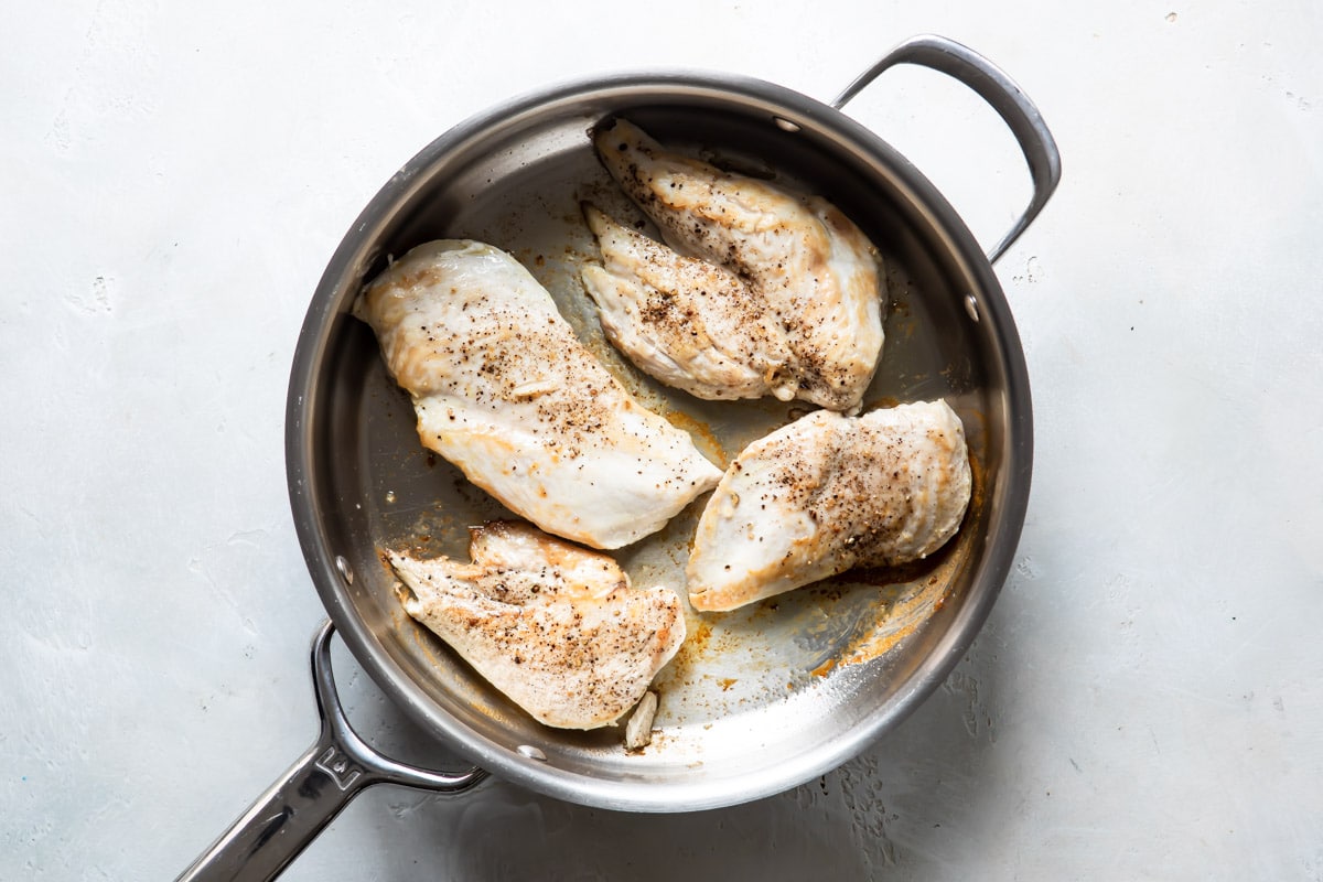 Chicken breasts being cooked in a silver skillet for chicken vesuvio.