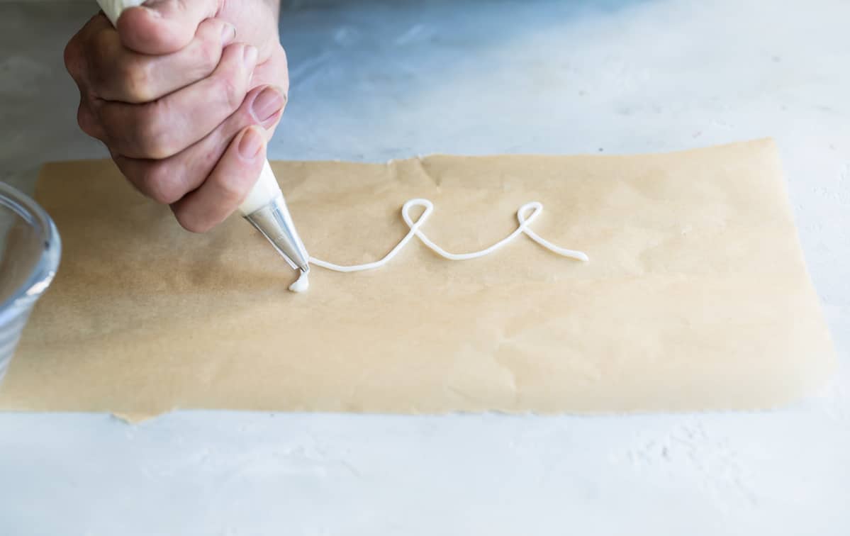 Someone practicing white piping swirls on a brown piece of parchment paper.