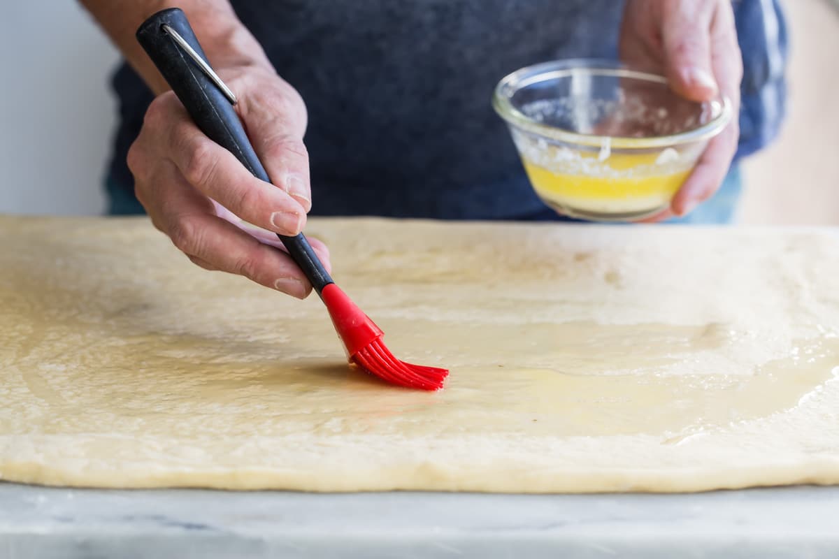 Brushing butter on rolled out cinnamon roll dough.