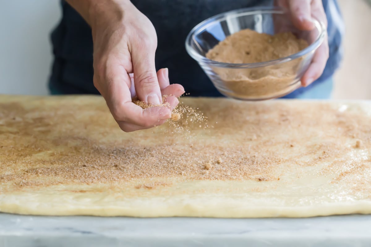 Sprinkling cinnamon roll dough with filling.