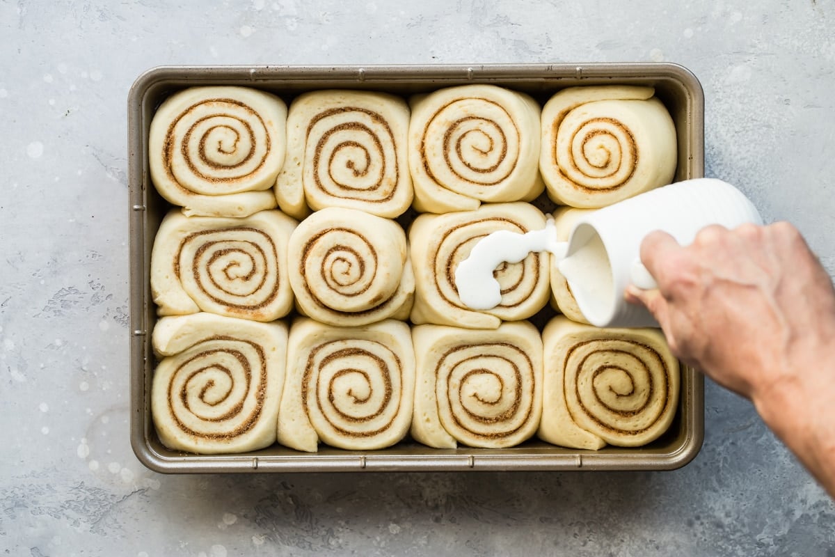 Someone pouring glaze over unbaked cinnamon rolls.