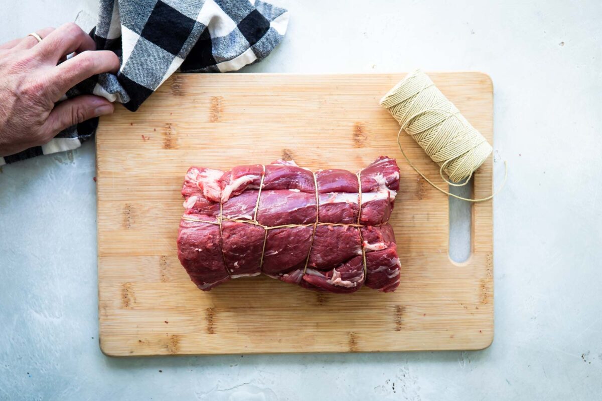 A beef tenderloin tied on a wooden cutting board.