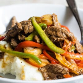 Midwest pepper steak over mashed potatoes in a white bowl.
