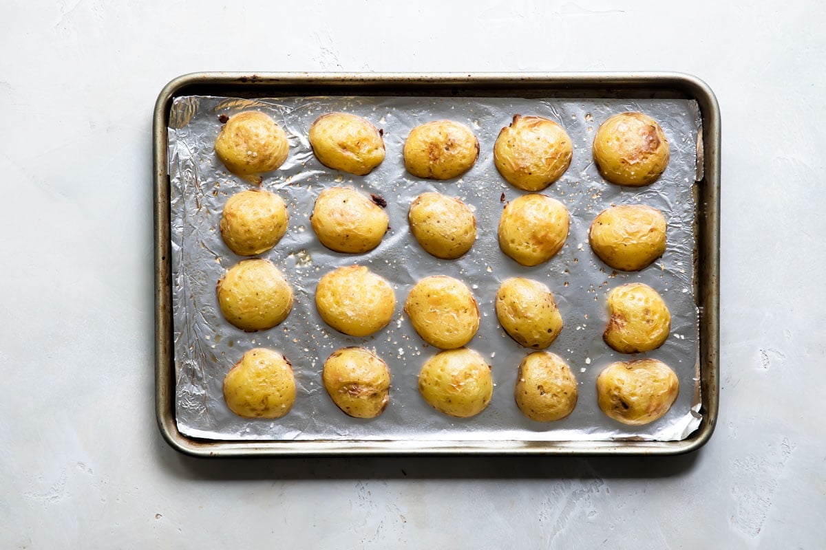 Mini potatoes face down on a baking sheet.