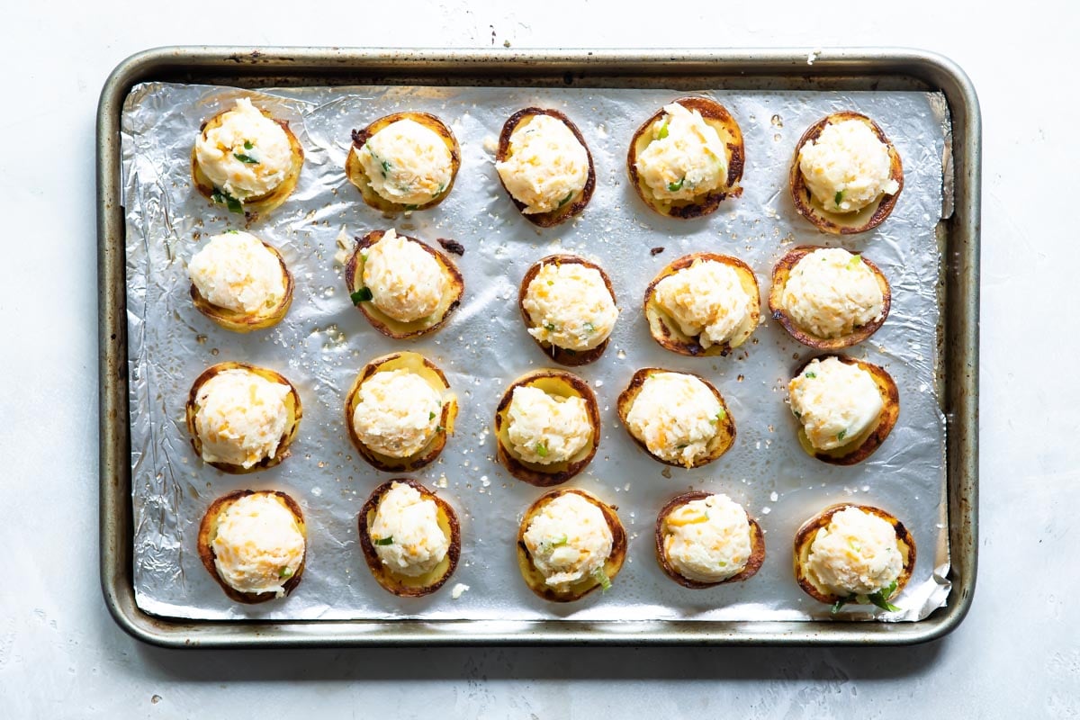 Mini twice baked potatoes on a silver baking sheet before being baked a second time.