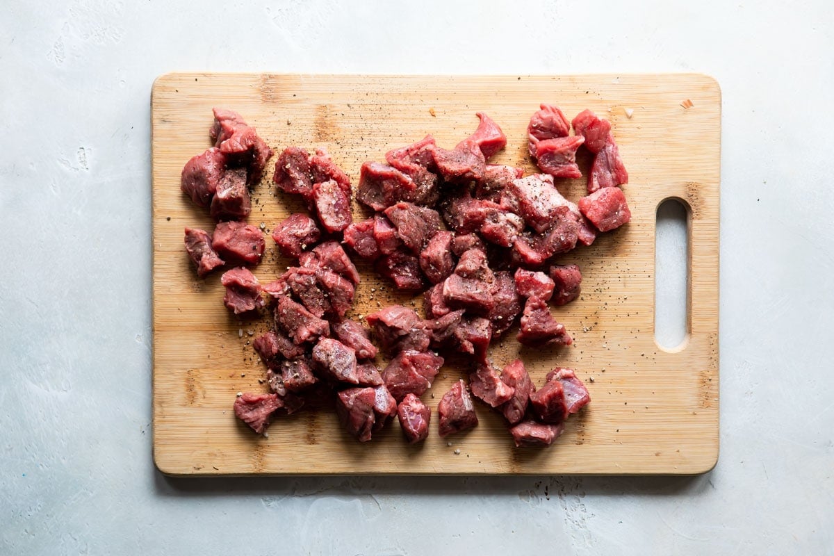 Seasoned beef pieces on a wooden cutting board.