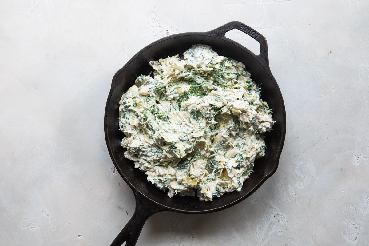 Spinach artichoke dip in a cast iron pan before being cooked.
