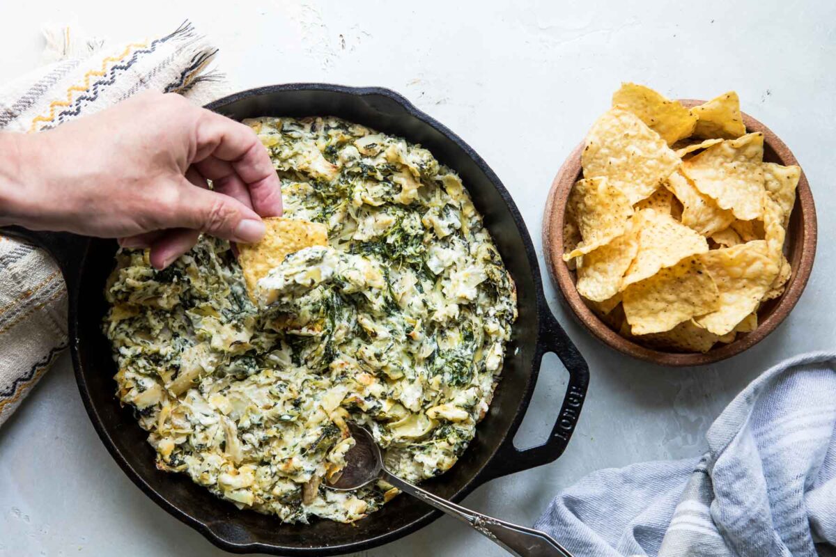 Someone dipping spinach artichoke dip out of a cast iron pan.