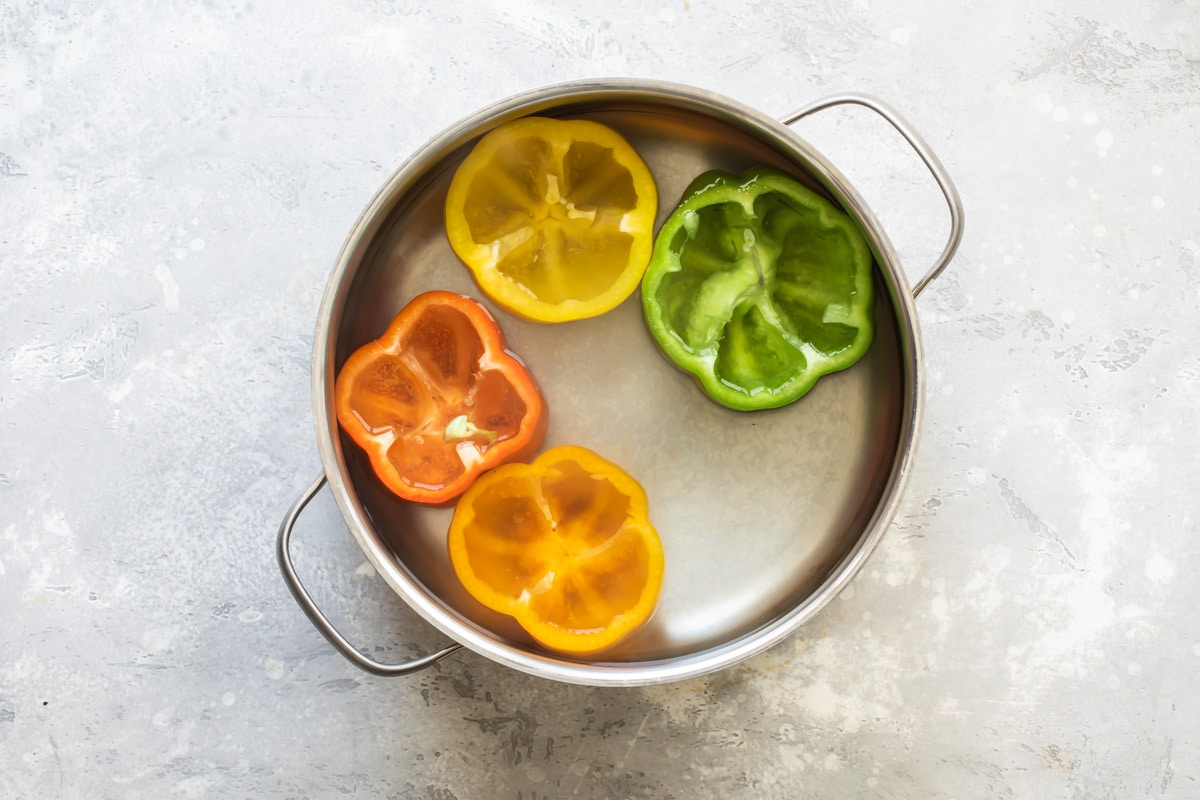 Four peppers with the tops cut off and cored in water in a sliver pot.