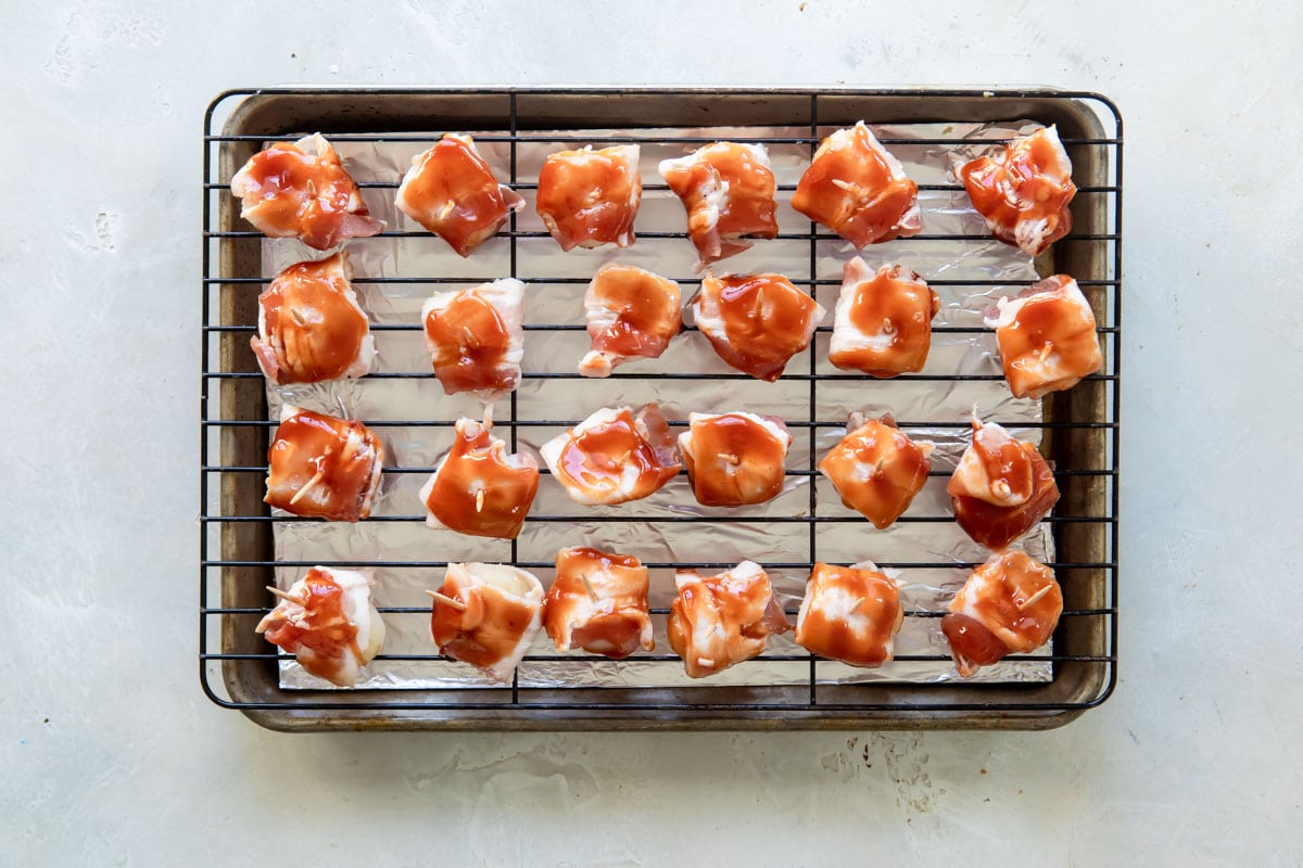 Bacon wrapped water chestnuts with barbecue sauce on a baking rack.