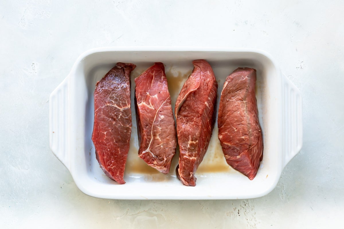 Four sirloin steak tip pieces in a baking dish.