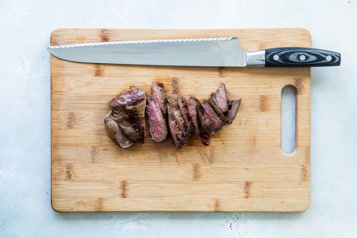 Sliced steak tips on a wooden cutting board with a knife.