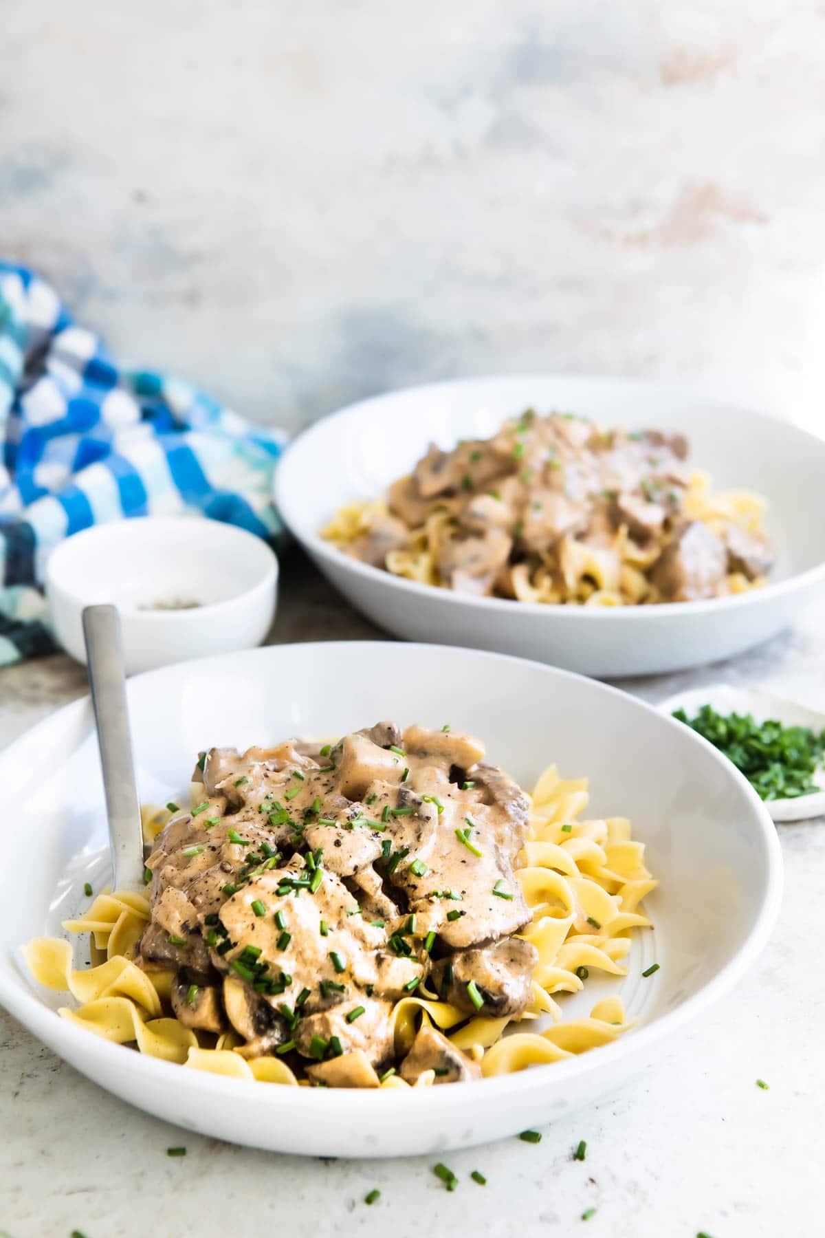 Beef stroganoff in a white bowl over egg noodles.