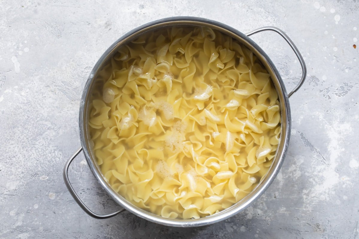 Boiled egg noodles and water in a silver stock pot.