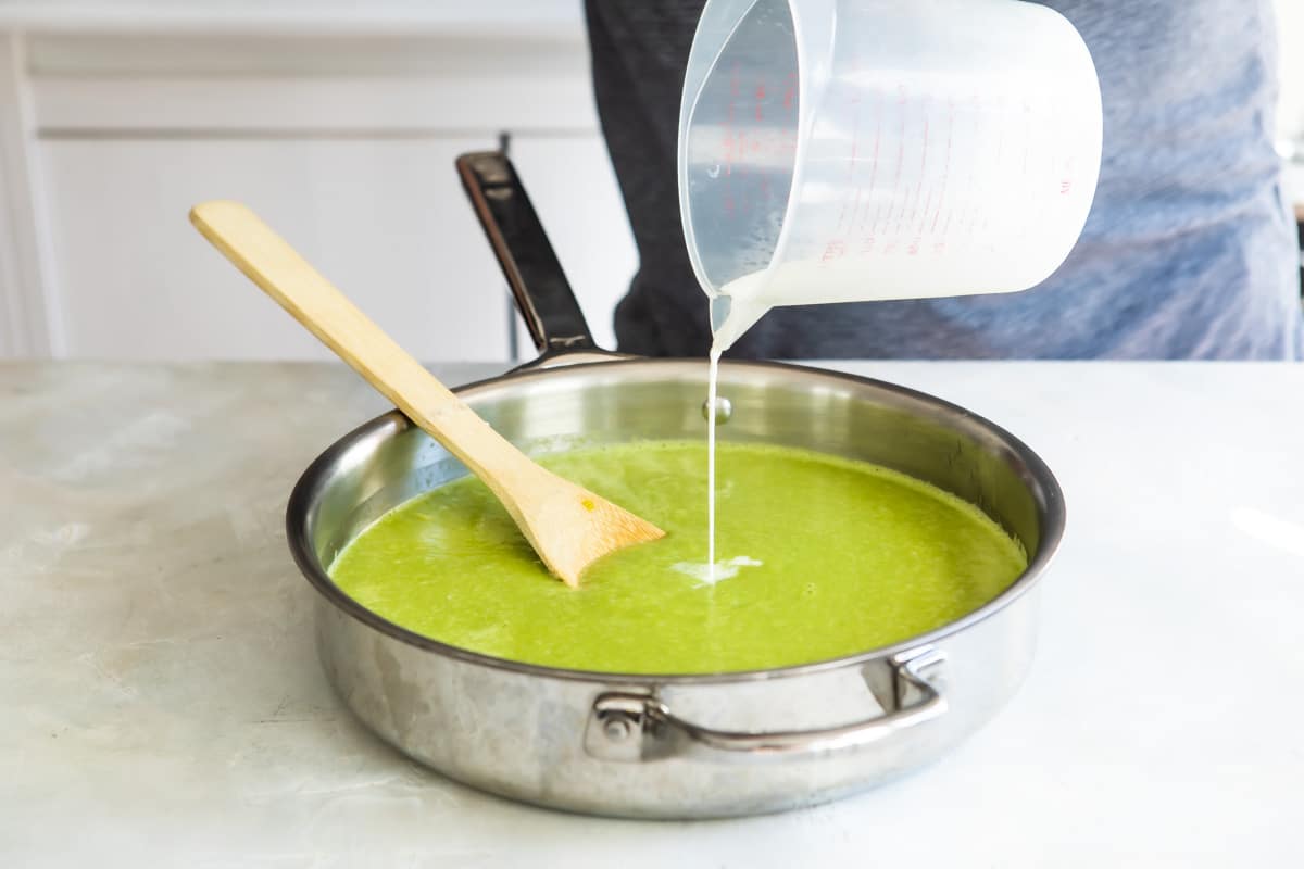 Adding cream to blended cream of asparagus soup.