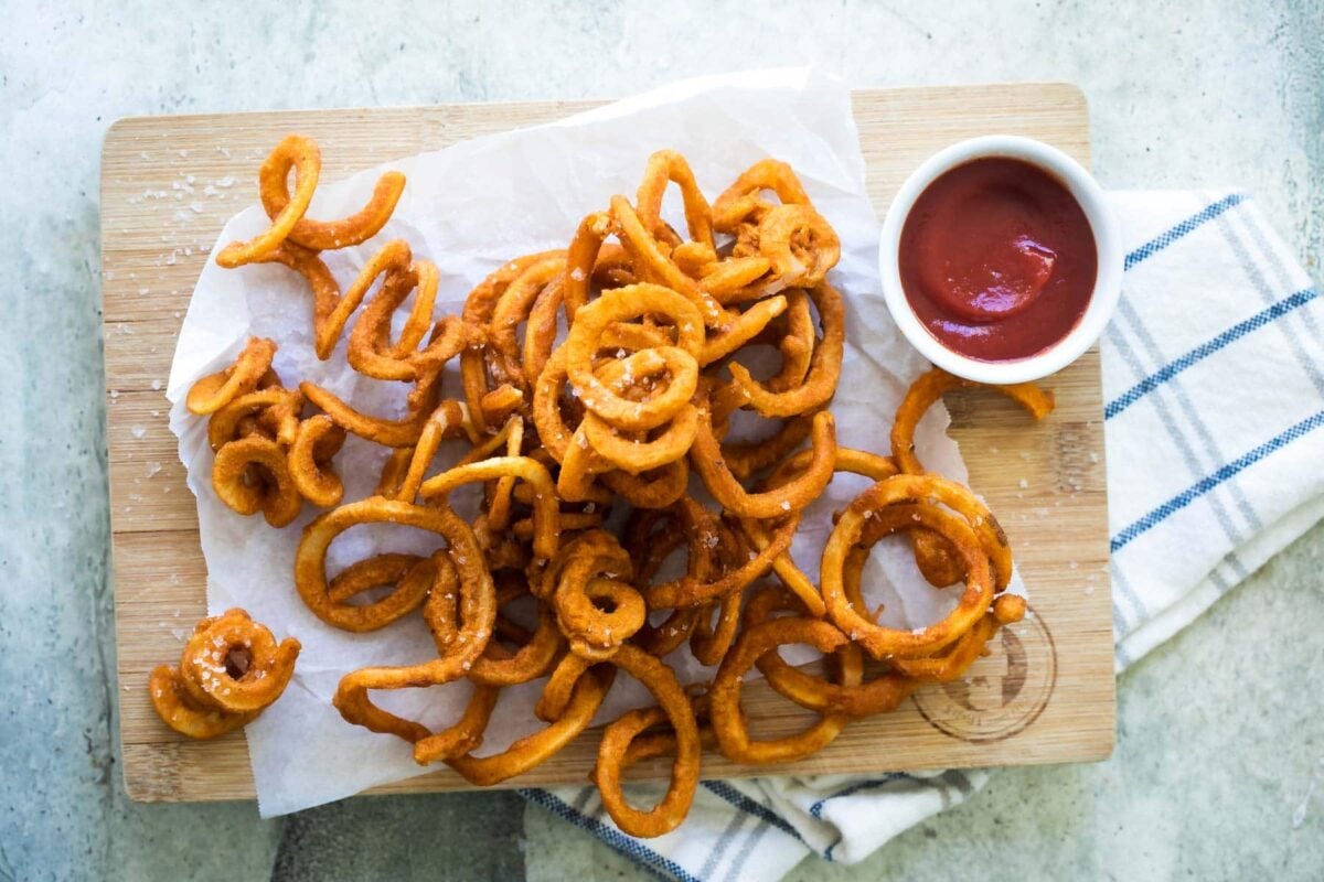 Curly fries on a wooden cutting board with a side of ketchup.