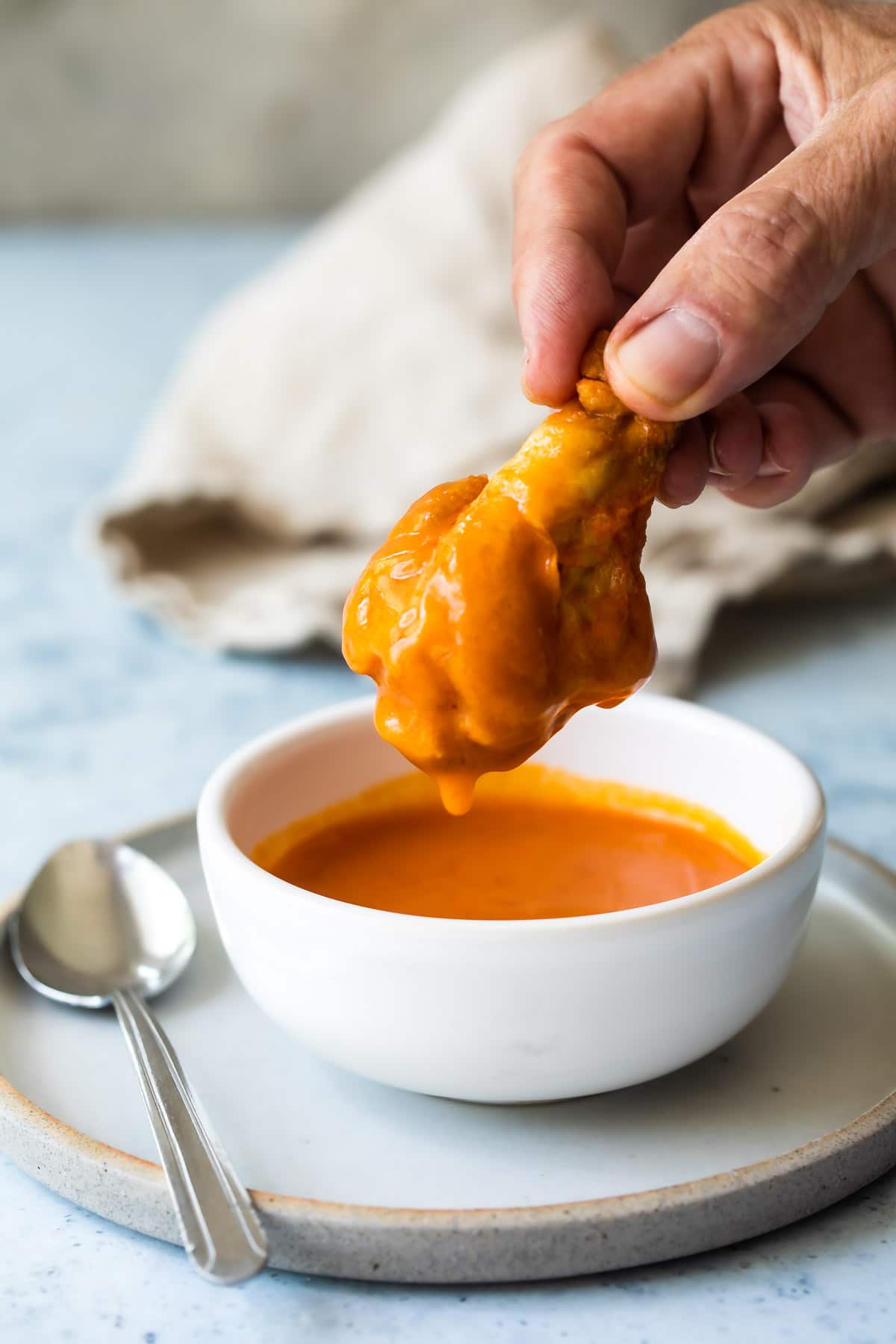 A chicken wing being dunked in buffalo sauce.