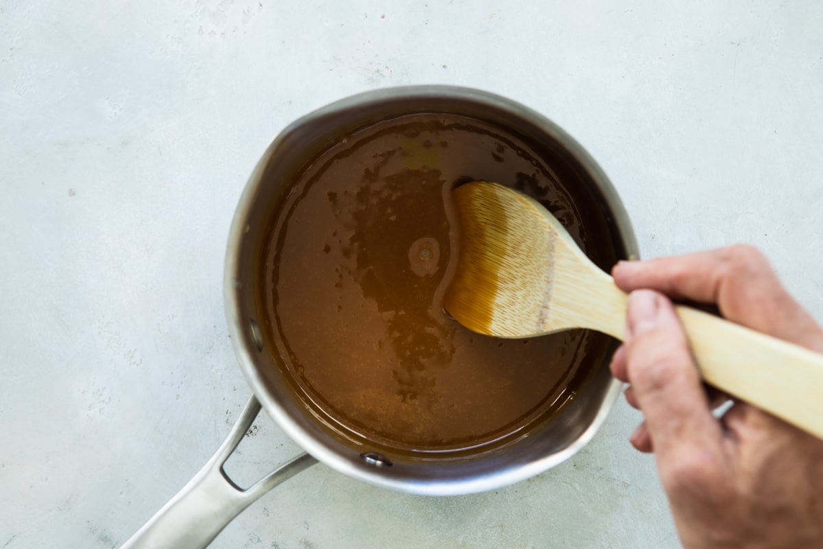 Someone stirring caramel in a silver saucepan.